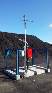 Yard spray dust suppression system structure. A spray hose is mounted to an underground tank near a pile of material.